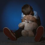 197144001-niño-triste-con-oso-de-peluche-cerca-de-la-pared-azul-concepto-de-violencia-doméstica