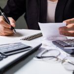 Stressed young woman checking bills, taxes, bank account balance and calculating expenses in the living room at home