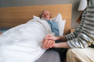 Close-up of unrecognizable loving young woman child holding hand of sick aged father lying in hospital bed.